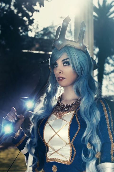 1girl ashe_(league_of_legends) ashe_(league_of_legends)_(cosplay) blue_eyes blue_hair bow cosplay crown female_focus ice league_of_legends long_hair looking_at_viewer makeup nail_polish outdoors photo_(medium) queen queen_ashe solo tree valentina_kryp weapon