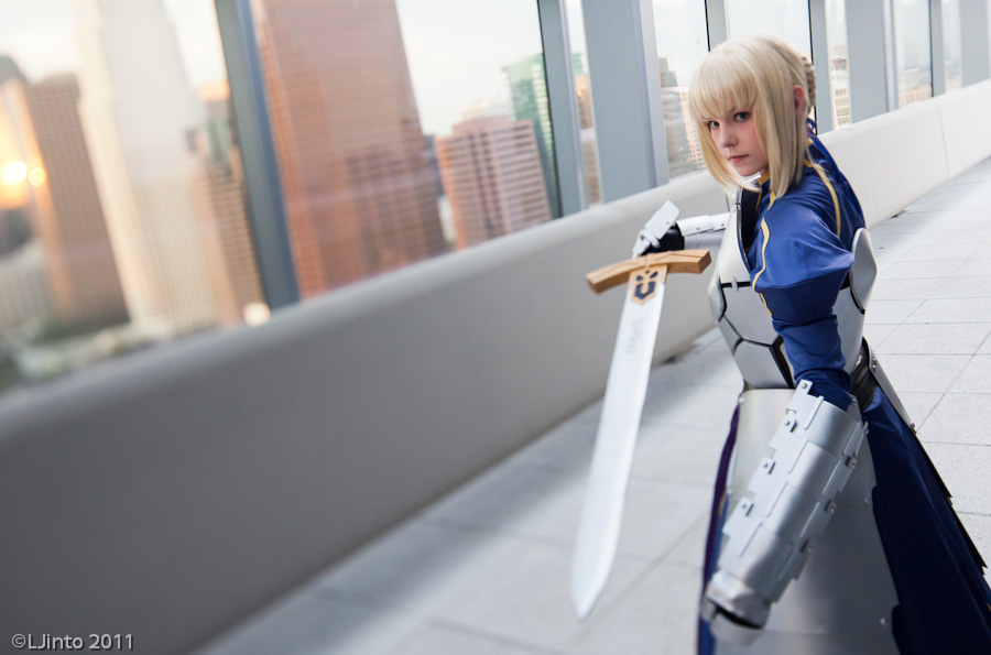 1girl armor armored_dress artoria_pendragon_(fate) blonde_hair building cosplay dress excalibur_(fate/stay_night) fate/stay_night fate/zero fate_(series) female_focus gauntlets green_eyes hair_ribbon maridah photo_(medium) ribbon saber_(fate) short_hair solo sword weapon