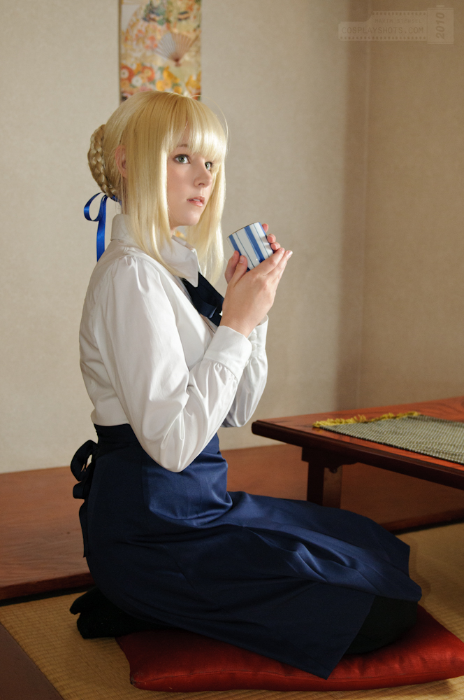 1girl ahoge artoria_pendragon_(fate) black_pantyhose blonde_hair blue_eyes braid cosplay cosplay_photo cup dress fate/stay_night fate_(series) female_focus hair_ribbon long_sleeves maridah pantyhose photo_(medium) pillow ribbon saber_(fate) saber_(fate)_(cosplay) seiza sitting solo table watermark