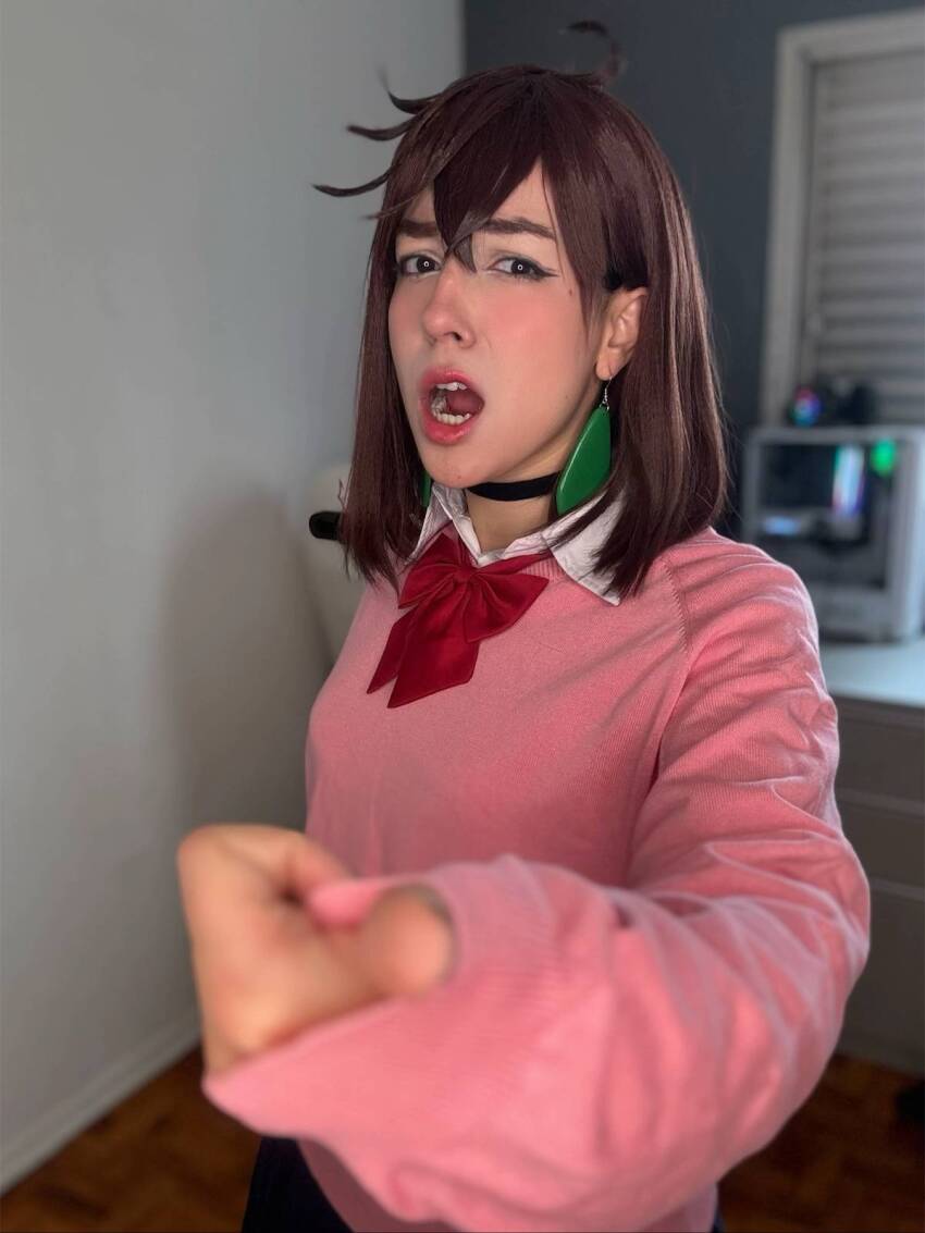 1girl ayase_momo ayase_momo_(cosplay) blurry blurry_background bow brazilian_(nationality) brown_hair cosplay dandadan female_focus highres indoors looking_at_viewer medium_hair nerokosplayer photo_(medium) pink_sweater red_bow skirt solo sweater teeth