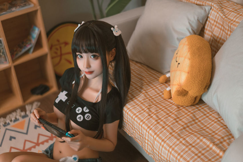 1girl asian bikini black_eyes black_hair box breasts chinese_(nationality) chunmomo0127 cleavage console crop_top denim denim_shorts indoors lips looking_at_viewer medium_breasts midriff nintendo_switch photo_(medium) pillow shorts solo stomach swimsuit tagme twintails underboob underwear video_game white_bikini