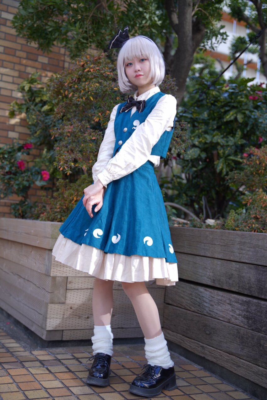 1girl aqua_eyes aqua_skirt aqua_vest black_bow black_bowtie black_hairband black_shoes bow bowtie closed_mouth collared_shirt cosplay_photo flower full_body grey_hair hairband highres hitodama_print konpaku_youmu long_sleeves outdoors pepe_peke photo_(medium) pigeon-toed pout print_skirt print_vest shirt shoes skirt skirt_set socks solo standing tile_floor tiles touhou tree vest white_shirt white_socks yellow_flower