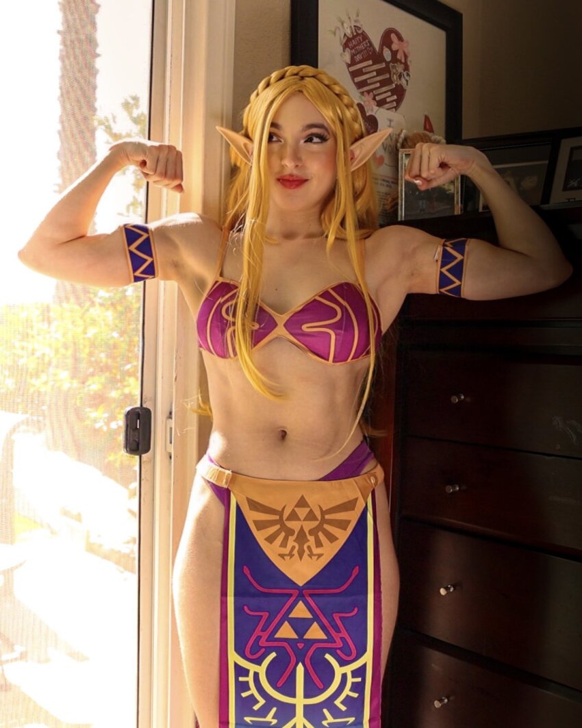 1girl 2023 abs alternate_costume arm_tattoo armband arms_up bare_shoulders bikini blonde_hair blue_eyes bra braid clenched_hands collarbone commentary cosplay cosplay_photo cowboy_shot crown_braid day dresser english_commentary female_focus fingernails flexing highres indoors loincloth long_fingernails missbrisolo navel nintendo panties parted_bangs parted_lips patterned_clothing photo_(medium) picture_frame pointy_ears princess_zelda princess_zelda_(cosplay) purple_bikini purple_bra purple_panties real_life red_lips sideways_glance solo stomach straight-on sunlight swimsuit tattoo the_legend_of_zelda the_legend_of_zelda:_breath_of_the_wild thick_lips thick_thighs thighs toned toned_female triforce_print underwear wrist_tattoo