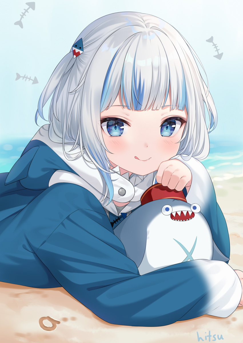 1girl :q a_(phrase) animal_hood beach bloop_(gawr_gura) blue_eyes blue_hair blue_hoodie blush closed_mouth commentary gawr_gura gawr_gura_(1st_costume) grey_hair hair_ornament highres hitsukuya hololive hololive_english hood hood_down hoodie looking_at_viewer lying multicolored_hair on_stomach sand shark_hair_ornament shark_hood sharp_teeth signature smile streaked_hair teeth tongue tongue_out two_side_up upper_body virtual_youtuber water