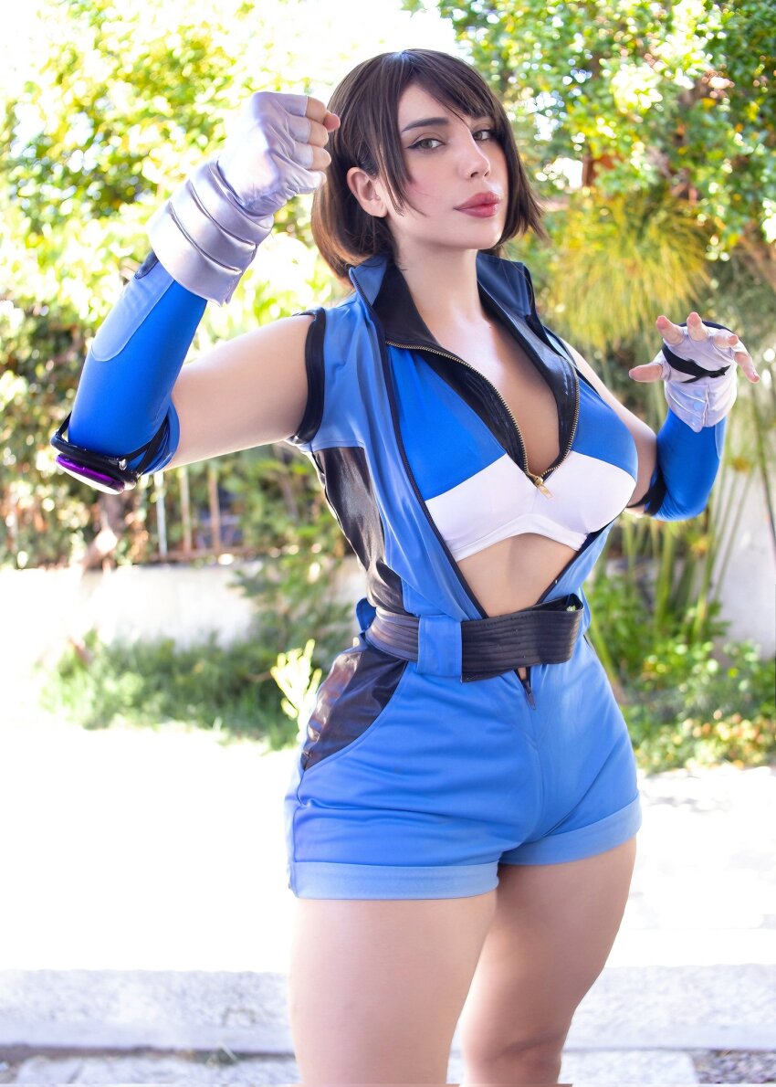 1girl 2025 armpit_peek arms_up backlighting belt belt_buckle blue_sports_bra blurry breasts brown_hair buckle clenched_hands collarbone commentary cosplay cosplay_photo day depth_of_field elbow_pads english_commentary female_focus fingerless_gloves full_body gloves hand_guard hands_on_own_hips high_collar highres kazama_asuka kazama_asuka_(cosplay) large_breasts looking_at_viewer missyle_fg namco outdoors photo_(medium) real_life short_hair sleeveless smile solo sports_bra standing tekken tekken_5 thick_lips thick_thighs thighs zipper zipper_pull_tab