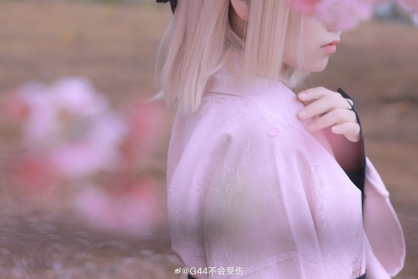 1girl absurdres artist_name blonde_hair blurry blurry_background blurry_foreground cherry_blossoms chinese_commentary close-up commentary_request cosplay cosplay_photo day depth_of_field fate/grand_order fate_(series) fingernails hand_up head_out_of_frame highres japanese_clothes jisi_si kimono koha-ace lips long_sleeves medium_hair nagatekkou okita_souji_(fate) okita_souji_(koha-ace) okita_souji_(koha-ace)_(cosplay) outdoors photo_(medium) pink_kimono print_kimono solo spring_(season) watermark weibo_watermark