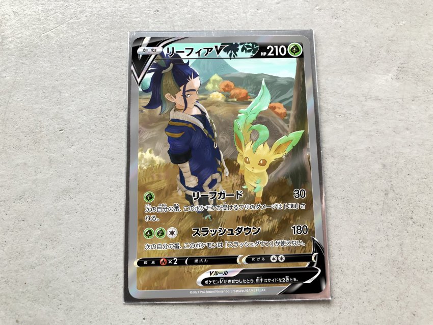 1boy adaman_(pokemon) arm_wrap blue_coat blue_hair card card_(medium) character_name character_print clenched_hand closed_mouth coat commentary_request day gen_4_pokemon grass green_hair highres leafeon male_focus mountain multicolored_hair nintendo official_style pokemon pokemon_legends:_arceus pokemon_tcg pokeyugami ponytail standing tree