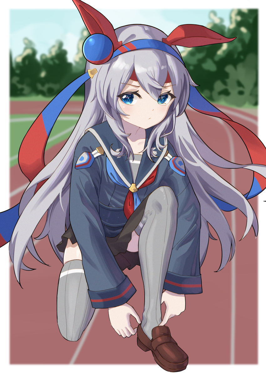 1girl absurdres adjusting_footwear animal_ears black_skirt blue_hairband blue_neckerchief blurry blurry_background brown_shoes chinese_commentary commentary_request depth_of_field ear_covers grey_hair grey_sailor_collar grey_shirt grey_thighhighs hair_between_eyes hairband headband highres horse_ears kneeling loafers long_hair long_sidelocks looking_at_viewer miniskirt neckerchief no_tail official_alternate_costume outdoors parted_bangs racetrack red_headband red_neckerchief ribbed_thighhighs sailor_collar school_uniform senbonsang serafuku shirt shoes sidelocks skirt solo tamamo_cross_(umamusume) thighhighs two-tone_neckerchief umamusume very_long_hair