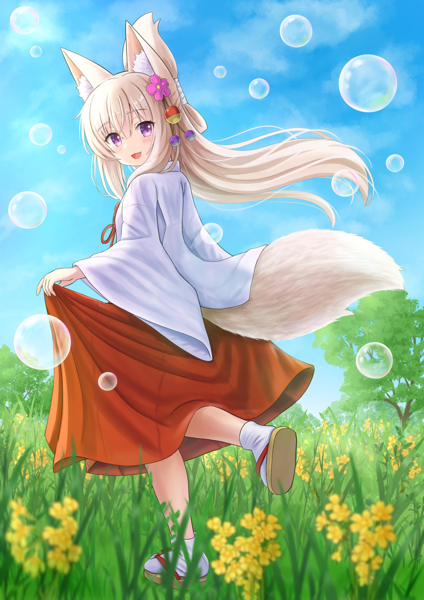 1girl :d absurdres animal_ear_fluff animal_ears blue_sky brown_hair brown_sandals bubble cloud commentary_request day flower folded_ponytail fox_ears fox_girl fox_tail grass hair_flower hair_ornament hakama hakama_hold highres iroha_(iroha_matsurika) japanese_clothes kimono koyoi_(iroha_(iroha_matsurika)) long_hair long_sleeves looking_at_viewer looking_to_the_side meadow miko open_mouth original outdoors pink_flower red_hakama sandals shoe_soles sky smile socks solo tabi tail tree very_long_hair white_kimono white_socks wide_sleeves yellow_flower zouri