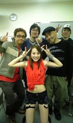  1girl 4boys asian baseball_cap brown_hair glasses god_knows grin happy hat hirano_aya indoors long_hair looking_at_viewer lowres midriff multiple_boys photo_(medium) real_life voice_actor shorts smile thumbs_up v wristband 
