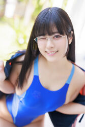 1girl black_hair blue_one-piece_swimsuit blurry blurry_background breasts glasses_on_head gravure_idol jacket japanese_(nationality) large_breasts looking_at_viewer medium_hair one-piece_swimsuit one_eye_closed open_clothes open_jacket outdoors photo_(medium) shinonome_umi smile solo swimsuit wink