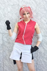 1girl ari arm_warmers bare_shoulders black_gloves cosplay eyelashes female_focus gloves green_eyes hand_up haruno_sakura haruno_sakura_(cosplay) head_tilt headband headdress highres holster konohagakure_symbol lips looking_at_viewer miniskirt naruto_(series) naruto_shippuuden photo_(medium) pink_hair red_shirt shirt short_hair shorts shorts_under_skirt side_slit skirt sleeveless sleeveless_shirt smile solo thigh_holster thigh_strap white_skirt