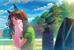 1girl animal_ears bag blurry blurry_foreground bottle brown_eyes brown_hair bug cloud dated day dragonfly ear_covers green_shirt hand_on_own_hip hand_up holding holding_towel horse_ears horse_girl insect king_halo_(umamusume) long_hair one_side_up open_mouth outdoors shirt short_sleeves solo sunlight sweat takuzui towel tree twitter_username umamusume v-shaped_eyebrows wiping_sweat