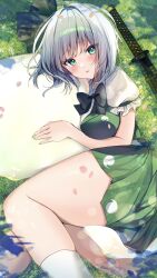 1girl between_thighs black_bow black_bowtie blush bow bowtie falling_petals ghost ghost_print green_eyes green_skirt green_vest grey_hair highres hitodama katana konpaku_youmu konpaku_youmu_(ghost) legs looking_at_viewer lying nenobi_(nenorium) on_grass parted_lips petals scabbard sheath short_hair skirt skirt_set socks solo sword thick_thighs thighs touhou vest wakizashi weapon white_socks