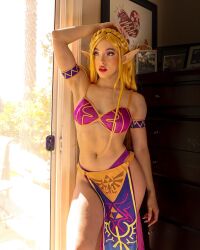 1girl 2023 abs alternate_costume arm_at_side arm_tattoo armband arms_up bare_shoulders bikini blonde_hair blue_eyes bra braid collarbone commentary contrapposto cosplay cosplay_photo cowboy_shot crown_braid day dresser english_commentary fingernails highres indoors loincloth long_fingernails looking_ahead missbrisolo navel nintendo panties parted_bangs parted_lips patterned_clothing photo_(medium) picture_frame pointy_ears princess_zelda princess_zelda_(cosplay) purple_bikini purple_bra purple_panties real_life red_lips stomach sunlight swimsuit tattoo the_legend_of_zelda the_legend_of_zelda:_breath_of_the_wild thick_lips thick_thighs thighs toned toned_female triforce_print underwear wrist_tattoo