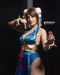 1girl alternate_costume argentine_(nationality) bare_hips bare_legs bare_shoulders blue_dress blue_eyes bracelet braid breasts brown_hair capcom chun-li chun-li_(cosplay) cleavage cosplay curvy double_bun dress fingernails hair_bun highleg highres instagram_username jewelry leotard leotard_under_clothes lips lipstick long_hair looking_at_viewer makeup medium_breasts no_bra pelvic_curtain photo_(medium) revealing_clothes shiny_clothes short_dress simple_background smile sophie_valentine spiked_bracelet spikes standing street_fighter street_fighter_iv_(series) thick_thighs thighs wide_hips