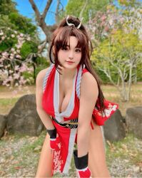 1girl breasts brown_hair chair cleavage cosplay cosplay_photo fatal_fury female_focus folding_chair hand_fan highres holding holding_fan large_breasts long_hair looking_at_viewer photo_(medium) ponytail real_life ririnacos shiranui_mai shiranui_mai_(cosplay) smile snk solo