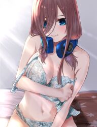 1girl arm_under_breasts blue_bra blue_eyes blue_panties blush bow bow_panties bra breasts brown_hair closed_mouth go-toubun_no_hanayome hair_between_eyes headphones headphones_around_neck lace lace_bra lace_panties large_breasts long_hair long_hair_between_eyes looking_at_viewer mitsugu morning nakano_miku navel on_bed panties sidelighting signature simple_background solo sunlight underwear underwear_only undone_bra white_background