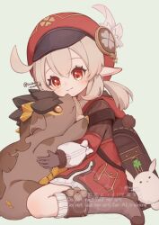 1girl ahoge backpack bag blonde_hair blush boots bow brown_bag brown_boots brown_gloves cabbie_hat charm_(object) closed_mouth commentary_request dodoco_(genshin_impact) dress genshin_impact gloves hair_between_eyes hat highres irohani_momiji klee_(genshin_impact) long_hair long_sleeves looking_at_another pointy_ears randoseru red_eyes red_hair sitting solo tepetlisaurus_(genshin_impact) twitter_username wariza white_bow