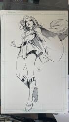 1girl belt black_lips black_shorts boots cape clenched_hands dan_mora dc_comics floating_cape greyscale grin highres legs long_hair long_sleeves looking_at_viewer marker_(medium) miniskirt monochrome photo_(medium) shorts signature skirt smile solo supergirl superhero_costume superman_(series) thighs toned toned_female traditional_media