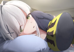 1girl absurdres bed_sheet black_hoodie blue_archive blush body_pillow breasts cleavage commentary_request cross_hair_ornament ganba_artworks green_eyes hair_intakes hair_ornament hair_over_one_eye hare_(blue_archive) highres hood hood_down hoodie indoors looking_at_viewer lying medium_breasts on_bed on_side parted_lips pillow sidelocks solo upper_body white_hair