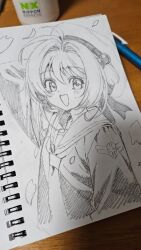 1girl :d antenna_hair arm_at_side arm_up art_tools_in_frame beret bob_cut cardcaptor_sakura commentary_request cropped_torso falling_petals flat_chest graphite_(medium) greyscale hair_bobbles hair_intakes hair_ornament hat highres kinomoto_sakura light_blush long_sleeves looking_at_viewer mechanical_pencil monochrome necktie one_side_up open_mouth pencil petals photo_(medium) sailor_collar sailor_shirt school_emblem school_uniform shirt short_hair shuri_(84k) sketchbook smile solo table tomoeda_elementary_school_uniform traditional_media winter_uniform wire_binding wooden_table