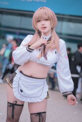 1girl apron bready_(nikke) cosplay crop_top goddess_of_victory:_nikke heart heart_print heeya_cos highres long_sleeves maid_apron multiple_others navel outdoors photo_(medium) real_life skirt thighhighs tongue tongue_out twintails