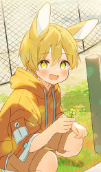 1boy animal_ears blonde_hair blush brown_shorts chain-link_fence child clover commentary_request double-parted_bangs drawstring far_tarooo fence four-leaf_clover grass highres holding holding_clover hood hood_down hoodie looking_at_viewer male_focus noru_(far_tarooo) open_mouth orange_hoodie original outdoors rabbit_boy rabbit_ears short_hair shorts smile solo squatting teeth upper_teeth_only yellow_eyes