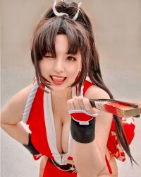 1girl breasts brown_hair cleavage cosplay cosplay_photo fatal_fury female_focus highres large_breasts long_hair looking_at_viewer one_eye_closed photo_(medium) ponytail real_life ririnacos shiranui_mai shiranui_mai_(cosplay) snk solo wink