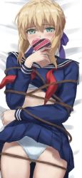 1girl artoria_pendragon_(fate) blonde_hair blue_sailor_collar blue_serafuku blue_shirt blue_skirt blush box bra bra_peek capsule_servant covered_mouth embarrassed fate/stay_night fate_(series) green_eyes heart-shaped_box highres long_sleeves looking_at_viewer lying miniskirt on_back on_bed panties pantyshot pleated_skirt rope saber_(fate) sailor_collar school_uniform serafuku shirt skirt solo tonee underwear valentine white_bra white_panties