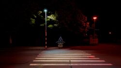 1girl black_hat chibi commentary crosswalk english_commentary full_body hat highres hololive hololive_english lamppost looking_at_viewer night phdpigeon photo_background pumpkin_costume railing real_world_location road sidewalk signpost smile smol_ame solo standing straight-on tree virtual_youtuber watson_amelia witch_hat zipper_pull_tab
